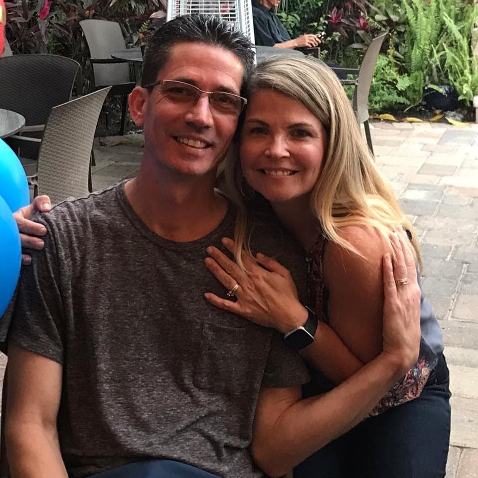 Smiling man in glasses and blonde woman posing closely together on an outdoor patio.
